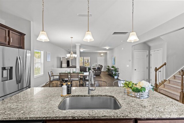 kitchen featuring stainless steel fridge, a sink, open floor plan, dark brown cabinets, and light stone countertops