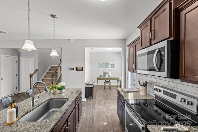 kitchen with stainless steel appliances, a sink, backsplash, pendant lighting, and light stone countertops