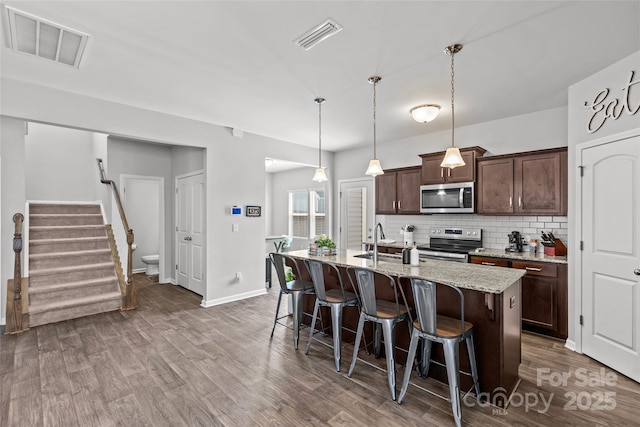 kitchen featuring appliances with stainless steel finishes, a kitchen breakfast bar, a sink, backsplash, and dark brown cabinets