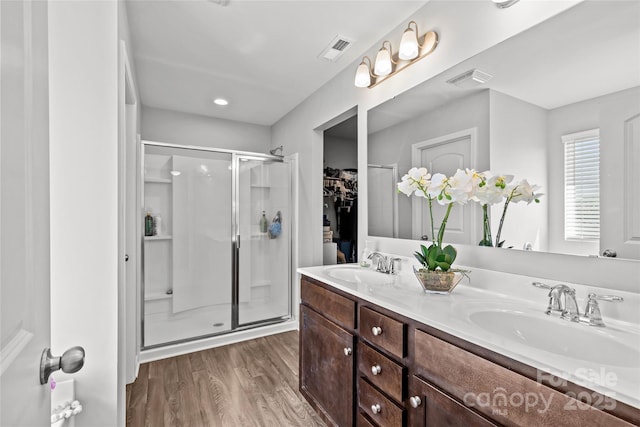 full bathroom with wood finished floors, a shower stall, double vanity, a walk in closet, and recessed lighting