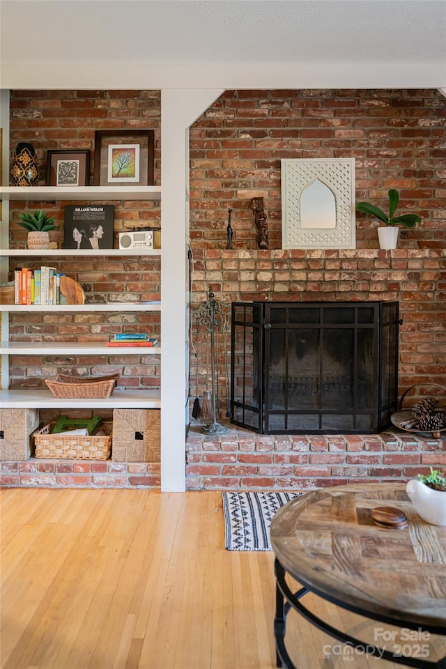 living room featuring wood-type flooring, a brick fireplace, and brick wall