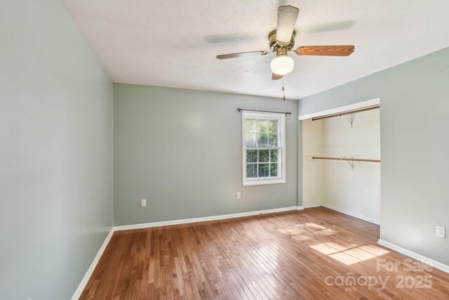 unfurnished bedroom featuring baseboards, ceiling fan, a closet, and wood finished floors