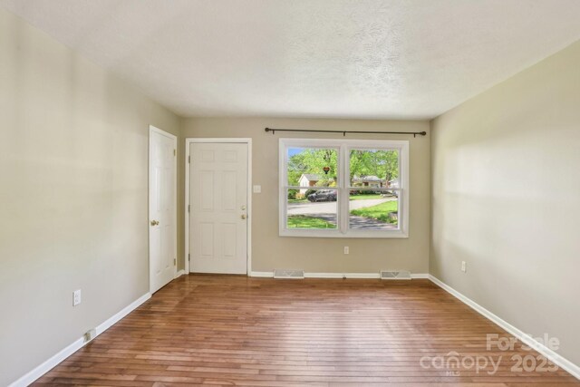 unfurnished room with baseboards, visible vents, and hardwood / wood-style floors