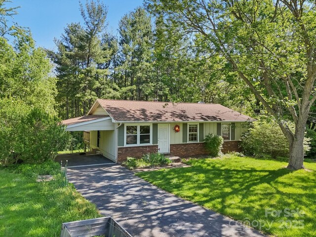 ranch-style house featuring roof with shingles, brick siding, a front yard, a carport, and driveway