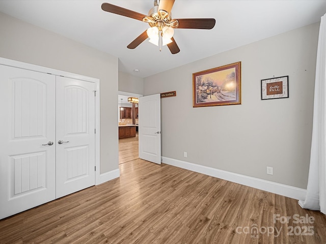 unfurnished bedroom with a closet, wood finished floors, baseboards, and a ceiling fan