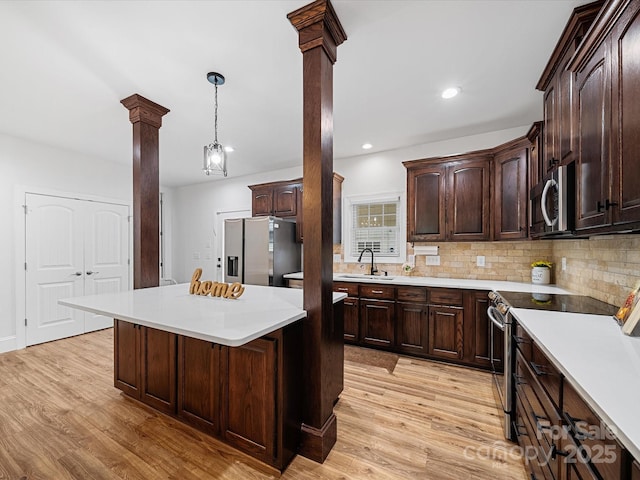 kitchen with decorative columns, stainless steel appliances, a sink, light countertops, and recessed lighting