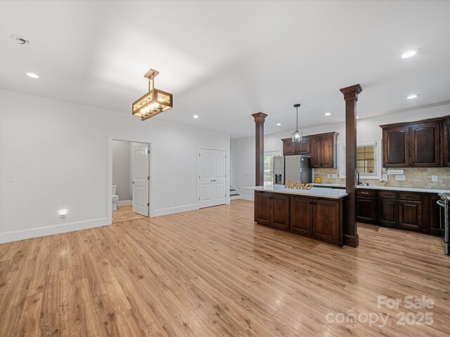 kitchen with ornate columns, stainless steel fridge, light countertops, dark brown cabinets, and light wood finished floors
