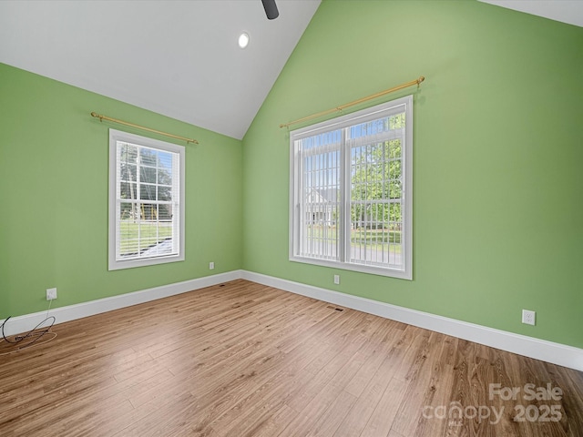 unfurnished room with healthy amount of natural light, baseboards, wood finished floors, and vaulted ceiling