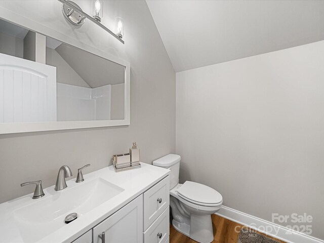 bathroom with vaulted ceiling, wood finished floors, toilet, and vanity