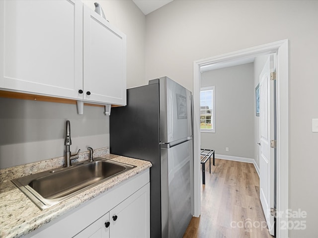 kitchen featuring a sink, freestanding refrigerator, light wood-style flooring, white cabinets, and light countertops
