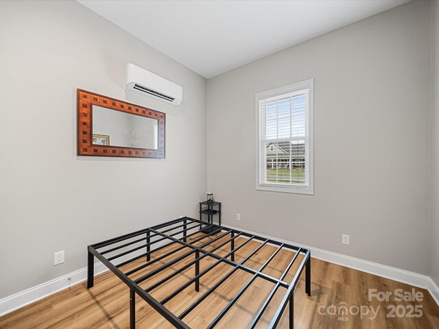unfurnished bedroom with an AC wall unit, baseboards, and wood finished floors