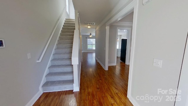 stairway with crown molding, baseboards, wood finished floors, and visible vents