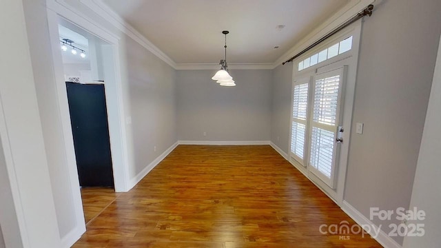 unfurnished dining area with baseboards, ornamental molding, and wood finished floors