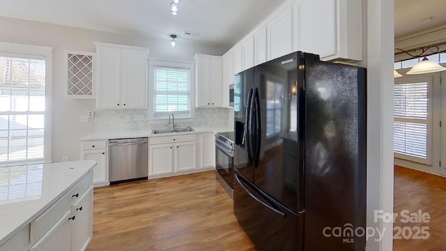 kitchen with white cabinets, appliances with stainless steel finishes, tasteful backsplash, a sink, and light wood-type flooring