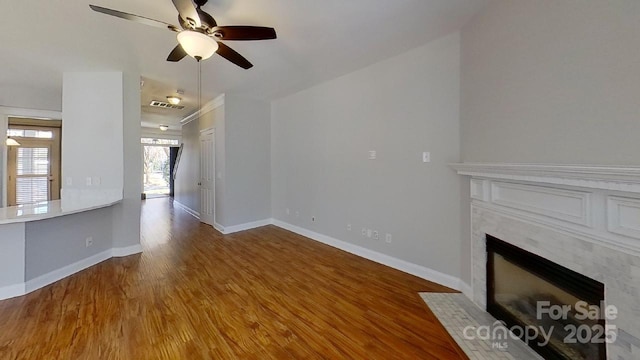 unfurnished living room with ceiling fan, visible vents, a fireplace, wood finished floors, and baseboards