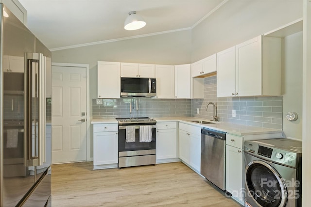 kitchen with vaulted ceiling, ornamental molding, a sink, appliances with stainless steel finishes, and washer / clothes dryer