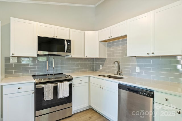 kitchen featuring white cabinets, stainless steel appliances, a sink, crown molding, and light countertops