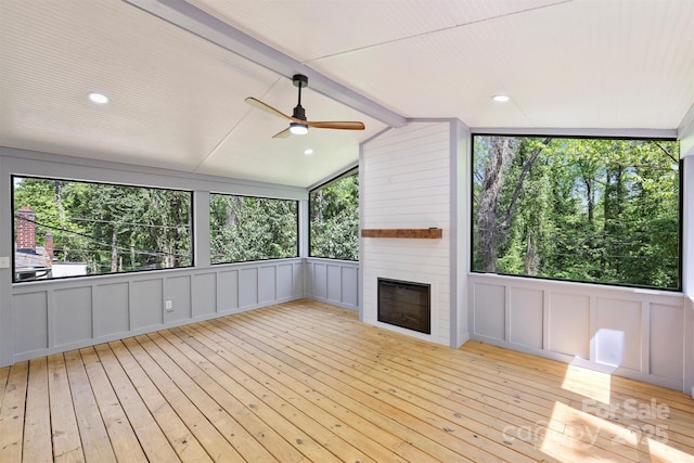 unfurnished sunroom featuring a ceiling fan, a large fireplace, and beamed ceiling