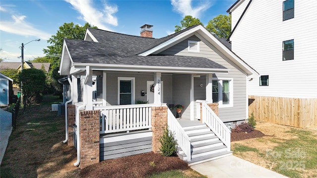 bungalow-style home featuring fence, a shingled roof, a chimney, and a porch