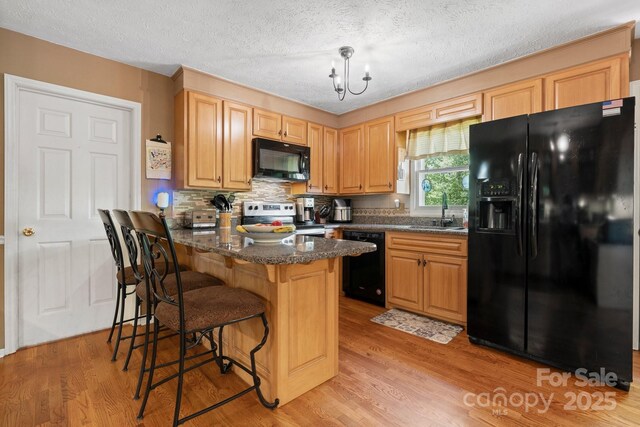 kitchen featuring a kitchen breakfast bar, a sink, black appliances, light wood finished floors, and a peninsula
