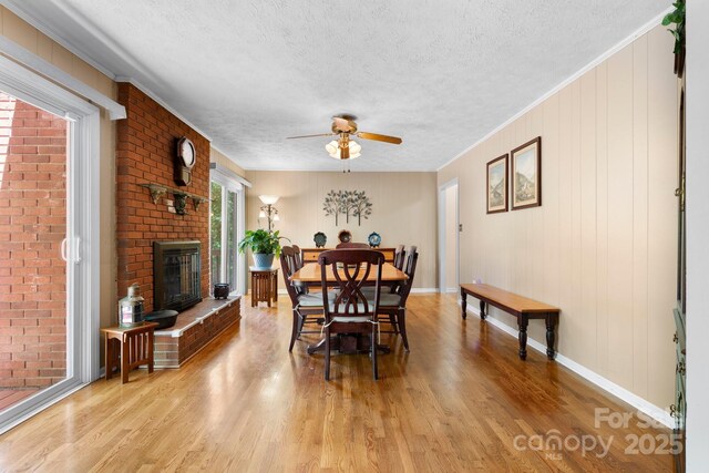 dining area with a textured ceiling, baseboards, light wood-style floors, ceiling fan, and a fireplace
