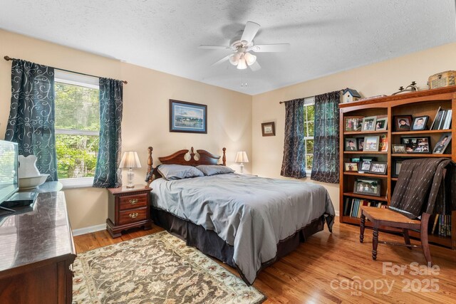 bedroom featuring ceiling fan, baseboards, a textured ceiling, and light wood-style flooring