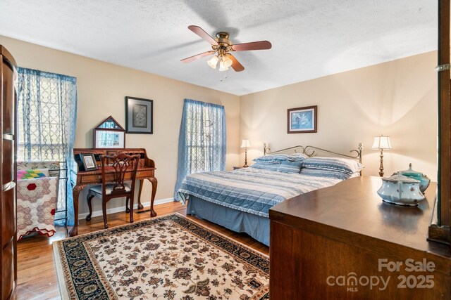 bedroom featuring baseboards, wood finished floors, a textured ceiling, and ceiling fan