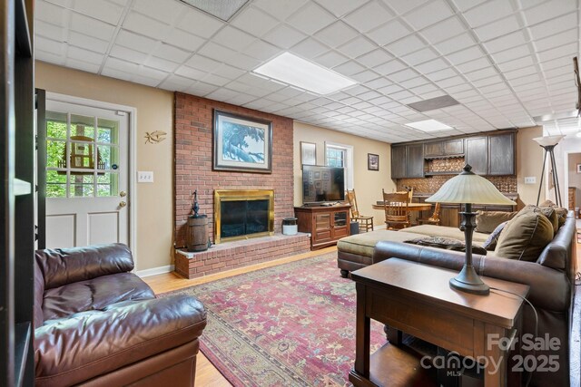 living area featuring light wood-style flooring, a brick fireplace, a drop ceiling, and a wealth of natural light
