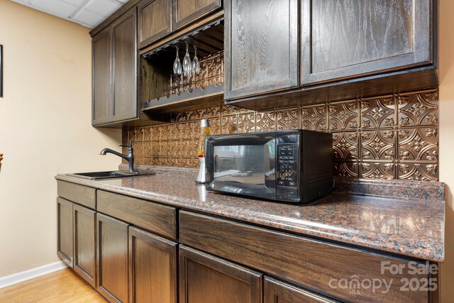 kitchen with a sink, decorative backsplash, black microwave, light wood-style floors, and dark brown cabinetry