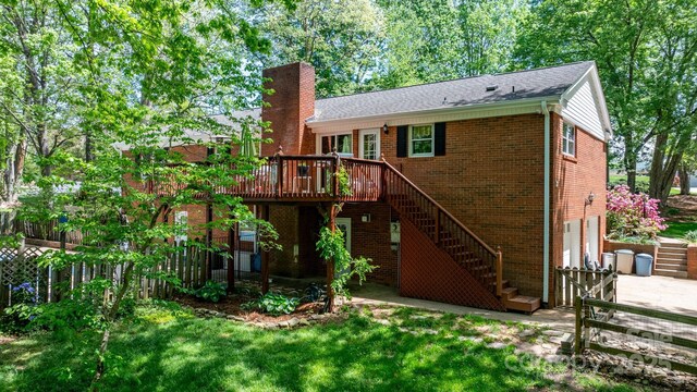 back of property featuring stairway, a chimney, a deck, brick siding, and a garage