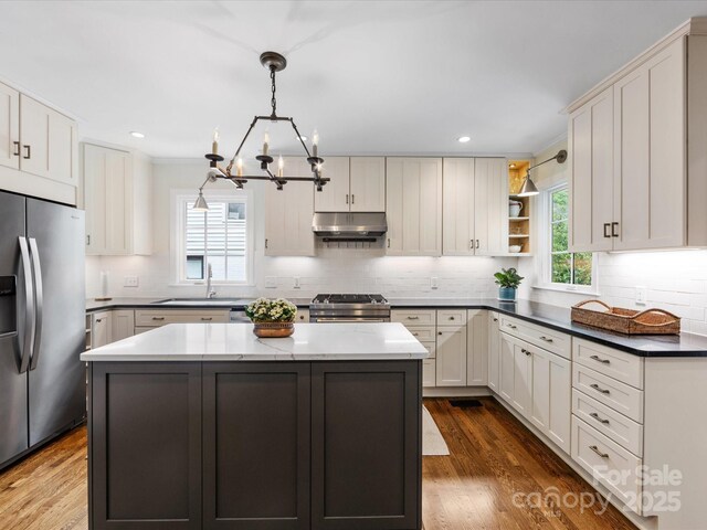 kitchen featuring a sink, under cabinet range hood, open shelves, a kitchen island, and appliances with stainless steel finishes