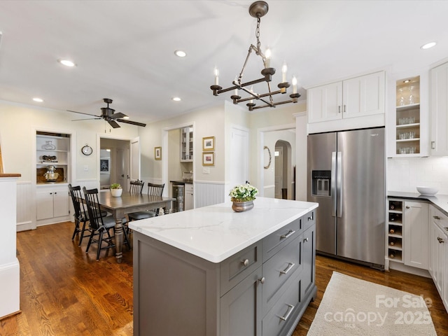 kitchen with white cabinets, a kitchen island, arched walkways, stainless steel fridge, and ceiling fan with notable chandelier