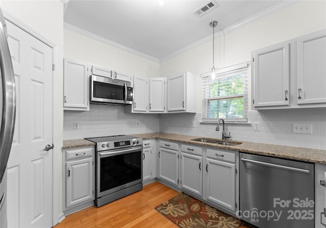 kitchen with a sink, light wood-type flooring, visible vents, appliances with stainless steel finishes, and ornamental molding