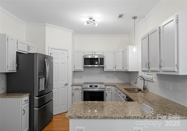 kitchen with a peninsula, a sink, visible vents, appliances with stainless steel finishes, and ornamental molding