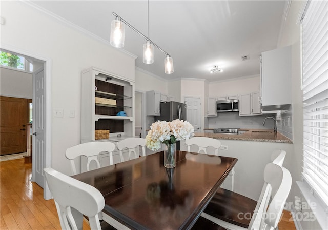 dining area with light wood-style flooring, visible vents, and crown molding