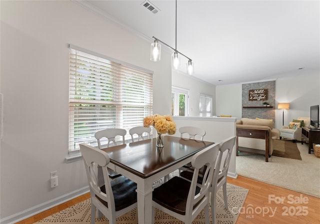 dining room featuring baseboards, light wood-style flooring, visible vents, and ornamental molding