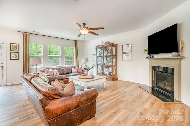 living room featuring a glass covered fireplace, light wood-style flooring, visible vents, and ceiling fan