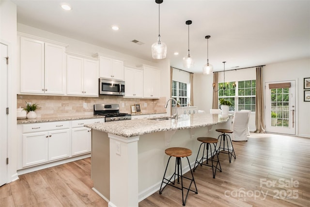 kitchen featuring tasteful backsplash, stainless steel appliances, visible vents, and light wood-style floors