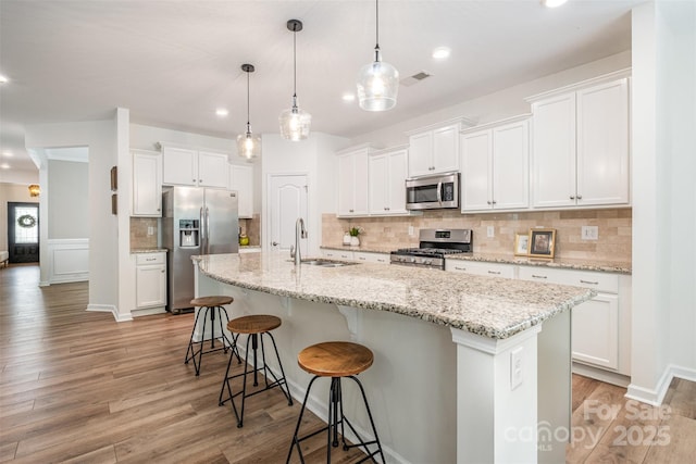 kitchen featuring a kitchen breakfast bar, visible vents, a sink, appliances with stainless steel finishes, and white cabinetry
