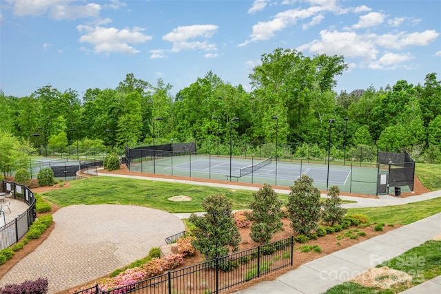 view of sport court featuring a yard, a wooded view, and fence