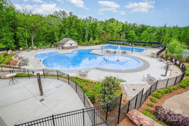 pool with a patio area, fence, and a view of trees