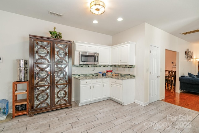 kitchen with visible vents, wood tiled floor, stainless steel microwave, white cabinets, and light stone counters