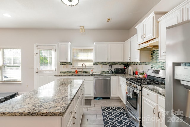 kitchen with white cabinets, appliances with stainless steel finishes, a sink, tasteful backsplash, and under cabinet range hood