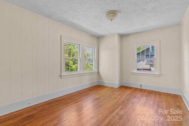 unfurnished room featuring baseboards, hardwood / wood-style flooring, and a textured ceiling