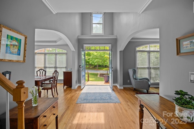 foyer entrance with arched walkways, baseboards, and light wood-style flooring