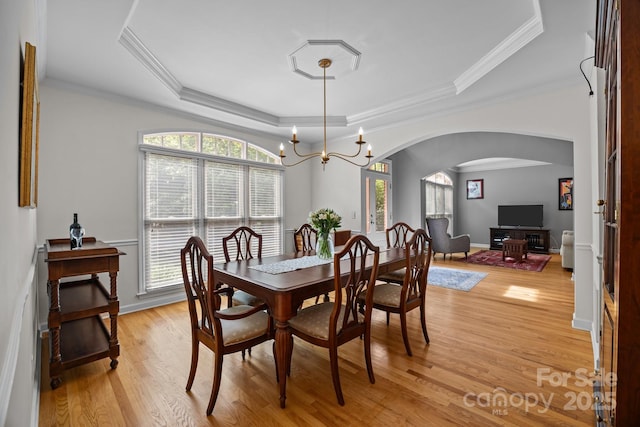 dining space featuring arched walkways, a tray ceiling, a healthy amount of sunlight, and light wood-style floors