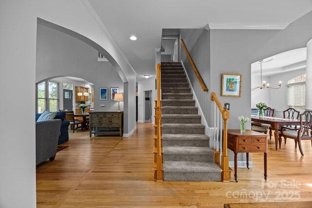 staircase with crown molding, arched walkways, wood finished floors, and an inviting chandelier