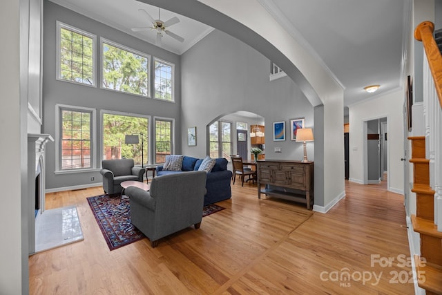 living room with ceiling fan, arched walkways, light wood-style flooring, baseboards, and ornamental molding