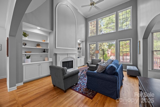 living area with a towering ceiling, arched walkways, light wood-type flooring, ornamental molding, and a premium fireplace