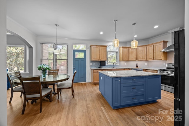 kitchen featuring crown molding, wall chimney range hood, a center island, light wood finished floors, and appliances with stainless steel finishes